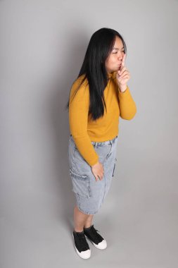 Güneydoğu Asyalı kadının üstten görünüşü. Gri arka planda tam boy giyinmiş, günlük sarı giyinmiş..