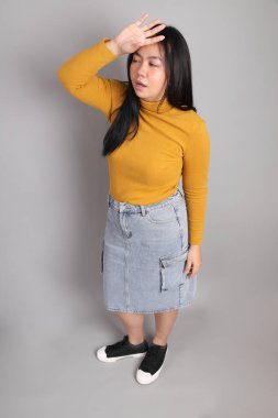 Güneydoğu Asyalı kadının üstten görünüşü. Gri arka planda tam boy giyinmiş, günlük sarı giyinmiş..