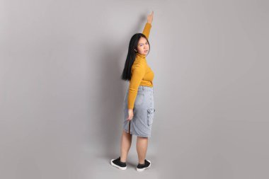 Gri arka planda duran Güneydoğu Asyalı kadının boyu.