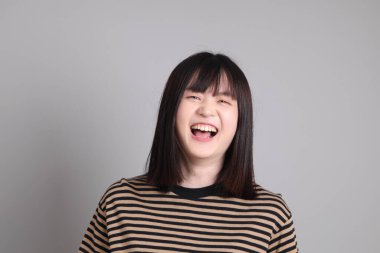 Gri arka planda duran genç Asyalı kadın.