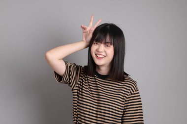 Gri arka planda duran genç Asyalı kadın.