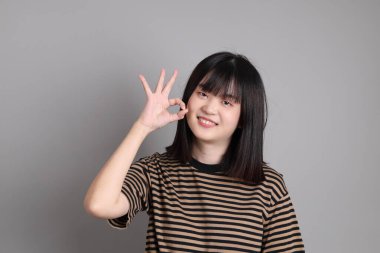 Gri arka planda duran genç Asyalı kadın.