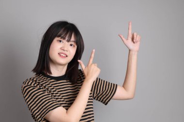 Gri arka planda duran genç Asyalı kadın.