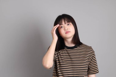 Gri arka planda duran genç Asyalı kadın.