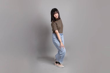 Gri arka planda duran genç, yetişkin Asyalı kadın..