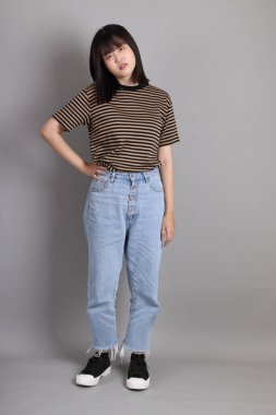 Gri arka planda duran genç, yetişkin Asyalı kadın..