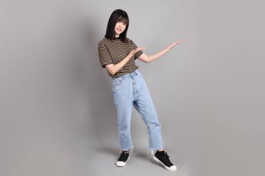 Gri arka planda duran genç, yetişkin Asyalı kadın..