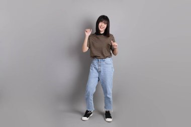 Gri arka planda duran genç, yetişkin Asyalı kadın..