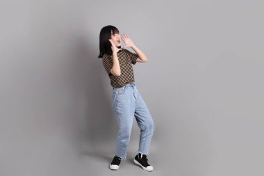 Gri arka planda duran genç, yetişkin Asyalı kadın..