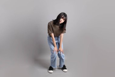 Gri arka planda duran genç, yetişkin Asyalı kadın..