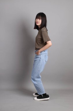 Gri arka planda duran genç, yetişkin Asyalı kadın..