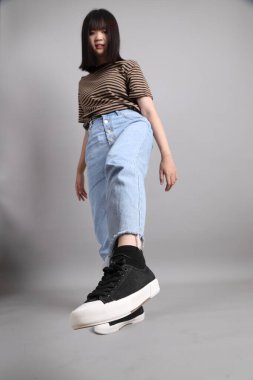 Gri arka planda duran genç, yetişkin Asyalı kadın..