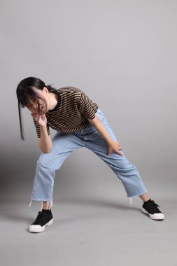 Gri arka planda duran genç, yetişkin Asyalı kadın..