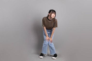 Gri arka planda duran genç, yetişkin Asyalı kadın..