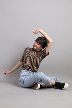 Gri arka planda duran genç, yetişkin Asyalı kadın..