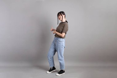 Gri arka planda duran genç, yetişkin Asyalı kadın..