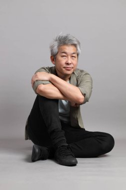 Gri arka planda oturan 40 'lı yaşlardaki Asyalı adam.. 