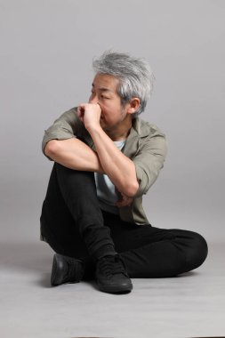 Gri arka planda oturan 40 'lı yaşlardaki Asyalı adam.. 