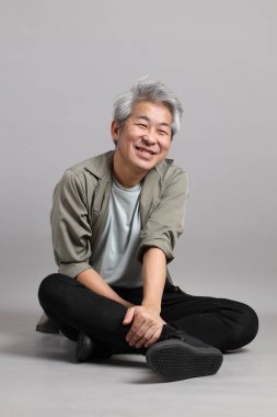 Gri arka planda oturan 40 'lı yaşlardaki Asyalı adam.. 