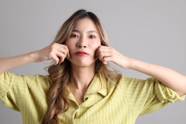 Gri arka planda sıradan giyinmiş Asyalı kadın..