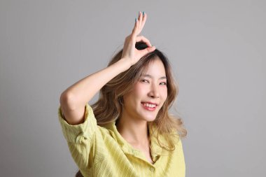 Gri arka planda sıradan giyinmiş Asyalı kadın..