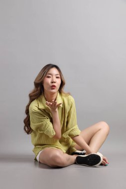 Gri arka planda oturan günlük giyinmiş Asyalı kadın..
