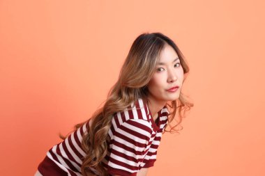 Turuncu arka planda duran ve poz veren sıradan giyinmiş genç Asyalı kadın. 