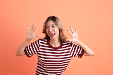 Turuncu arkaplanı işaret eden günlük giysili genç Asyalı kadın. 