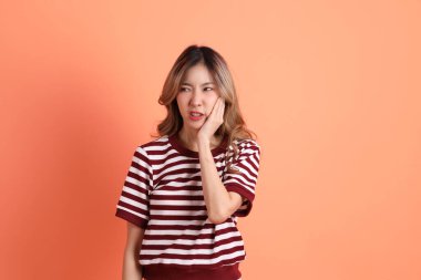 Turuncu arka planda diş ağrısı jesti yapan sıradan giyinmiş genç Asyalı kadın. 