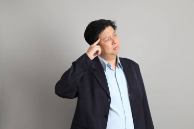 Resmi giyinmiş Asyalı iş adamı gri arka planda düşünce jesti yapıyor..