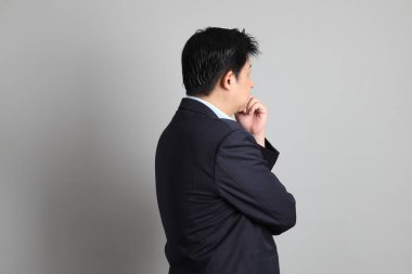 Resmi giyinmiş Asyalı iş adamı gri arka planda düşünce jesti yapıyor..