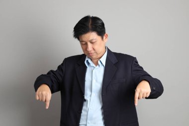 Gri arkaplanı işaret eden resmi giyinmiş Asyalı iş adamı..