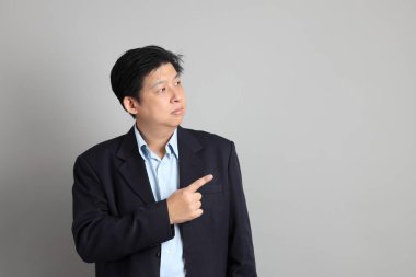 Gri arkaplanı işaret eden resmi giyinmiş Asyalı iş adamı..