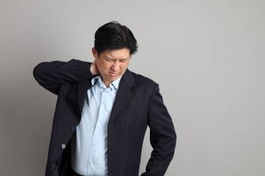 Resmi giyinmiş Asyalı iş adamı. Gri arka planda bitkin bir jestle..