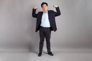 Asyalı iş adamı. Gri arka planda güçlü ve sağlıklı bir jestle resmi giyinmiş..