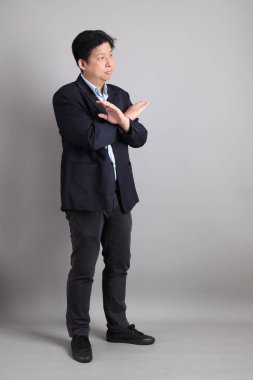 Asyalı iş adamı, resmi giyinmiş. Gri arka planı reddediyor, yasaklıyor, durduruyor..