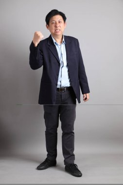 Resmi giyinmiş, neşeli, heyecanlı, gri arka planda kutlama yapan Asyalı iş adamı..