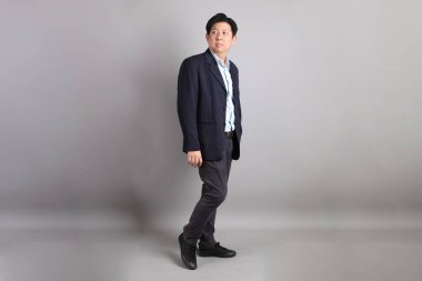 Resmi giyinmiş, gri arka planda duran Asyalı iş adamı..