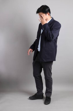 Gri arka planda Uykucu hareketi ile resmi giyinmiş Asyalı iş adamı..