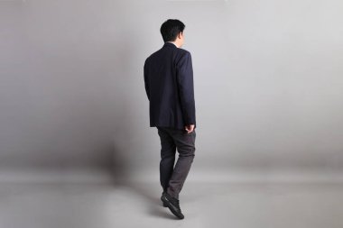 Resmi giyinmiş, gri arka planda duran Asyalı iş adamı..