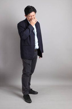 Resmi giyinmiş Asyalı iş adamı. Gri arka planda hastalıklı hareketler yapıyor..