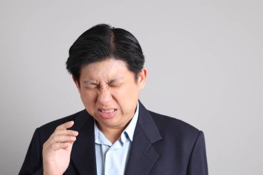 Gri arka planda baş ağrısı jesti ile resmi giyinmiş Asyalı iş adamı..