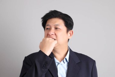 Tembellik jesti ve gri arka planda ciddi olmayan resmi giyinmiş Asyalı iş adamı..