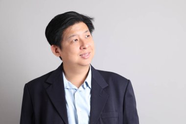 Resmi giyinmiş, gri arka planda duran Asyalı iş adamı..