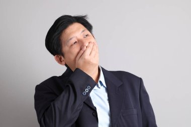 Resmi giyinmiş Asyalı iş adamı. Gri arka planda hastalıklı hareketler yapıyor..