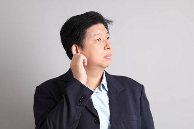 Tembellik jesti ve gri arka planda ciddi olmayan resmi giyinmiş Asyalı iş adamı..