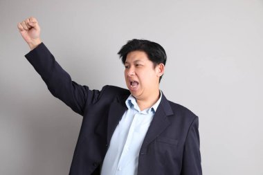 Resmi giyinmiş, neşeli, heyecanlı, gri arka planda kutlama yapan Asyalı iş adamı..