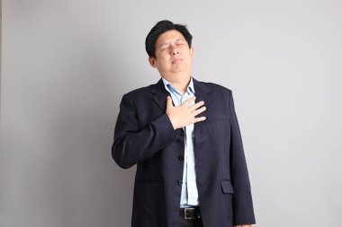 Gri arka planda Heartache jesti ile resmi giyinmiş Asyalı iş adamı..