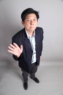 Asyalı iş adamı, resmi giyinmiş. Gri arka planı reddediyor, yasaklıyor, durduruyor..