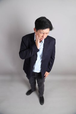 Gri arka planda diş ağrısı jesti ile resmi giyinmiş Asyalı iş adamı..